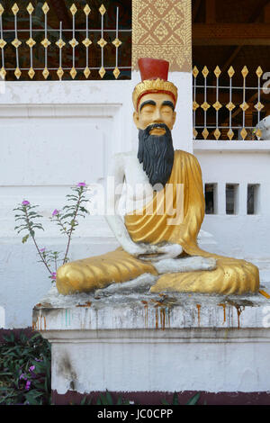 Männliche Figur außerhalb des Hauptgebäudes eines Wat komplexe sitzt, Luang Prabang, Laos Stockfoto