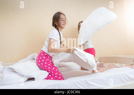 Zwei Mädchen im Schlafanzug kämpfen mit Kissen auf Bett Stockfoto