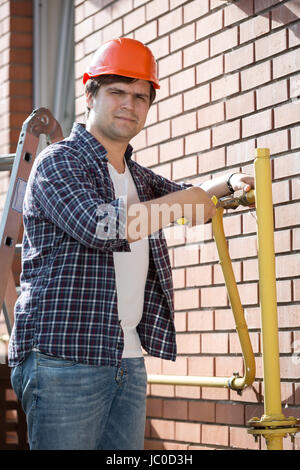 Porträt des jungen Klempners Bauarbeiterhelm Aufrechterhaltung gelbe Gasleitungen außerhalb des Hauses Stockfoto