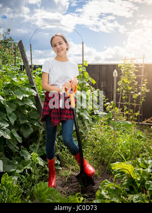 Lächelnd junges Mädchen in Gummistiefel halten Schaufel und arbeiten im Garten Stockfoto