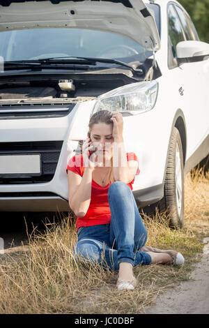 Jung betonte Frau an dem kaputten Auto am Straßenrand sitzen und im Gespräch per Telefon Stockfoto