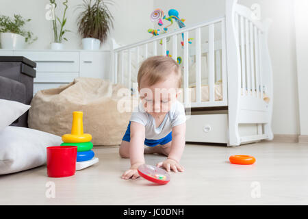 Entzückende Baby junge spielt auf Boden mit bunten Ringen von Spielzeug Pyramide Turm Stockfoto