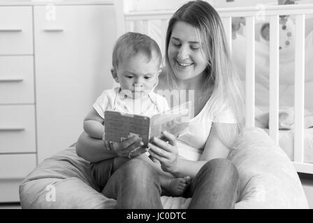 Schwarz / weiß Porträt der junge fröhlich Mutter mit Baby im Sitzsack sitzen und lesen Buch Stockfoto