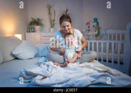 Liebevolle Mutter Windeln für ihr Baby Sohn auf Bett in der Nacht Stockfoto