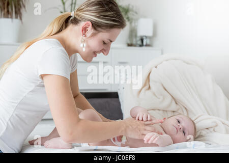 Porträt der glückliche junge Mutter ihr Baby Windeln auf Bett Stockfoto