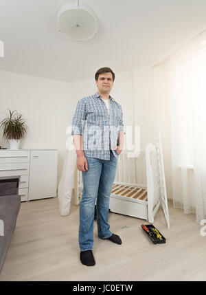 Junger Mann in Jeans und Shirt posiert im Schlafzimmer mit zerlegten Möbel Stockfoto