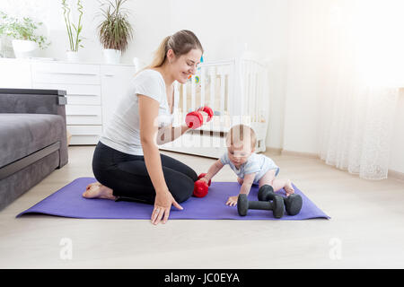 Schöne lächelnde Mutter mit ihrem Baby auf Boden mit Hanteln trainieren Stockfoto