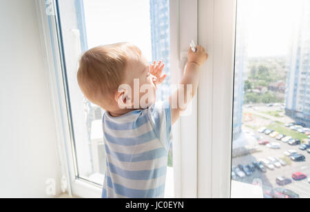 Baby in Gefahr. Baby Boy Handle des Fensters ziehen Stockfoto