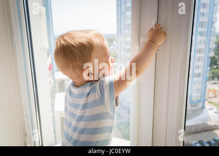 Baby in Gefahr. Kleines Baby versucht, öffnen Sie Fenster und ziehen den Griff Stockfoto