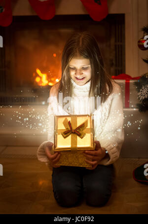 Porträt von glücklich lächelnde Mädchen glänzend Weihnachts-Geschenk-Box zu öffnen. Licht und Funken fliegen Auspacken Stockfoto