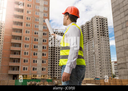 Rückansicht auf Architekt in Bauarbeiterhelm zeigen mit gerollten Baupläne im Gebäude im Bau Stockfoto