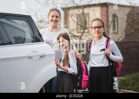 Porträt von glückliche Mutter und zwei Mädchen mit Schulranzen posiert am Auto Stockfoto