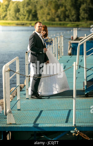 In voller Länge Portrait von Braut und Bräutigam umarmt auf Pier am Fluss Stockfoto