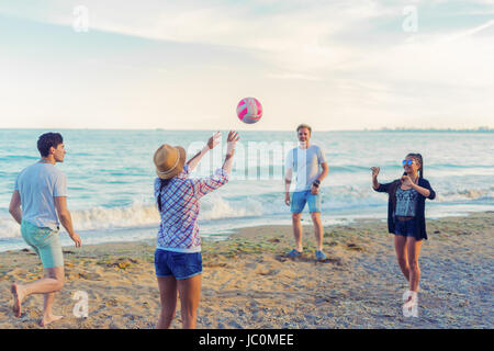 Freunde spielen Volleyball am wilden Strand bei Sonnenuntergang Stockfoto