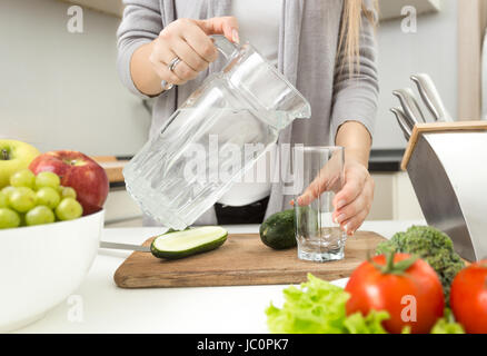 Nahaufnahme Foto Frau gießt Wasser in Glas in der Küche Stockfoto