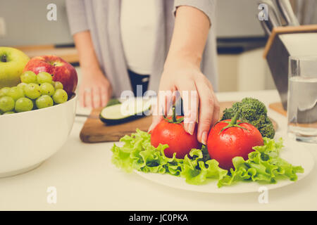 Closeup getönten Foto Frau Kommissionierung frischen Tomaten vom Tisch in der Küche Stockfoto