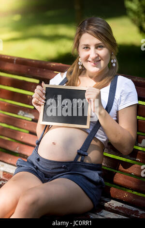 Süß lächelnd schwangere Frau hält Tafel mit Text "Es ist ein Junge" Stockfoto