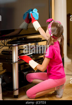 Kleines Mädchen in Gummihandschuhe TV Bildschirm staubfrei mit blauem Tuch reinigen Stockfoto