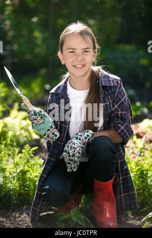 Porträt von niedlichen lächelndes Mädchen Handschuhe und Gummistiefel posiert im Garten Stockfoto