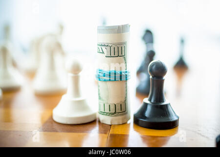 Closeup konzeptionelle Foto verdrehten Dollarscheine auf Schachbrett zwischen weißen und schwarzen Stücke stehen Stockfoto