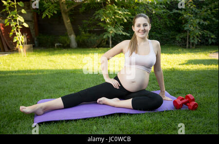 Freudige schwangere Frau stretching auf dem Rasen im Park am sonnigen Tag Stockfoto