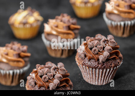 Hintergrund der Schokoladen Cupcakes garniert mit Schokolade-Chips und Schokolade Zuckerguss auf schwarzem Hintergrund Stockfoto