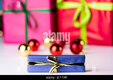 Glitzer Kugeln und Bowknots in soft-Fokus bringen die scharfen Konturen der blauen eingewickelt Gegenwart mit der goldenen Schleife vorne. Stockfoto