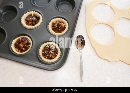 Mince Pies machen in der Küche - gefüllte Gebäck Fällen, Hackfleisch, Teig Fetzen und Teelöffel Stockfoto