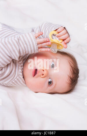 Babymädchen mit Puppe liegt auf einer weißen Decke Stockfoto