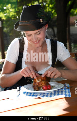 Blonde Mädchen isst halbe Hähnchen in einem traditionellen bayerischen Biergarten Stockfoto