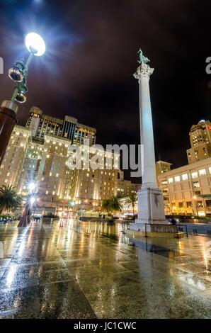 Eine Nacht-Blick auf den Union Square in der Innenstadt von San Francisco, California, Vereinigte Staaten von Amerika. Ein Wahrzeichen der Gegend mit einer Spalte mit einer Statue des Sieges hält einen Dreizack im Herzen des Stadtzentrums an der Spitze. Stockfoto