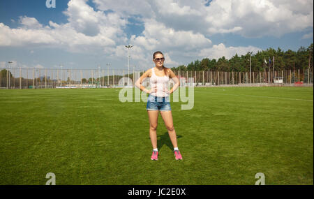 Schöne schlanke Frau steht auf Fußballplatz am sonnigen Tag Stockfoto