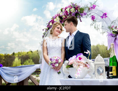Schöne Braut und Bräutigam stehen unter floral Bogen an sonnigen Tag Stockfoto