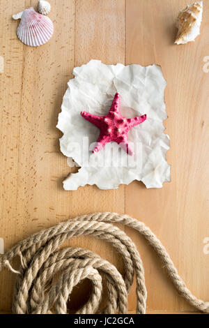 Rote Seestern auf liegend Stück der alten Papier auf Holzbohlen mit Muscheln und Seil Stockfoto