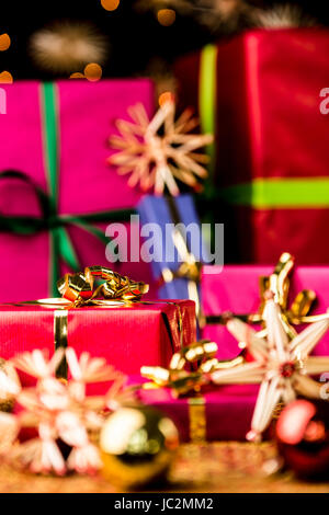 Sechs Weihnachtsgeschenke in monochromen Geschenkverpackungen. Fokus ist auf dem Goldenen Bogen rund um das kleine purpurrote rote Geschenk auf der linken Seite eingestellt. Kugeln und Sterne sind außerhalb der geringen Schärfentiefe. Stockfoto