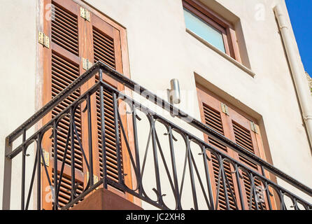 Fragment einer Fassade des alten Hauses an der Küste der Insel Kreta mit einem Balkon und alten hölzernen Jalousien vor der Sonne. Stockfoto