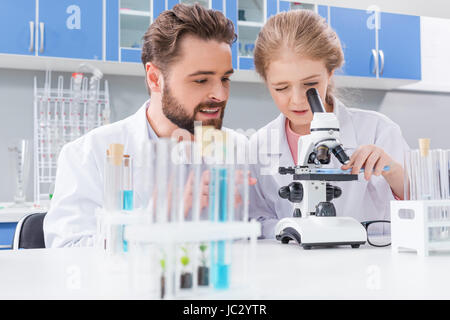 Lächelnd bärtige Lehrer betrachten kleine Schüler arbeiten mit Mikroskop im Labor Stockfoto