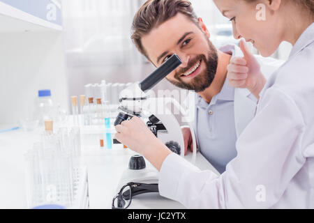 Lächelnd bärtige Lehrer betrachten kleine Schüler arbeiten mit Mikroskop im Labor Stockfoto