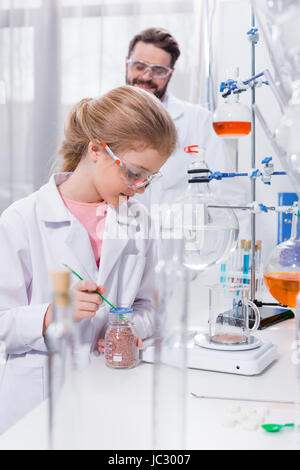 Lächelnd bärtige Lehrer betrachten kleine Schüler machen Experiment im Labor Stockfoto