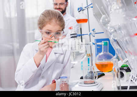 Lächelnd bärtige Lehrer betrachten kleine Schüler machen Experiment im Labor Stockfoto