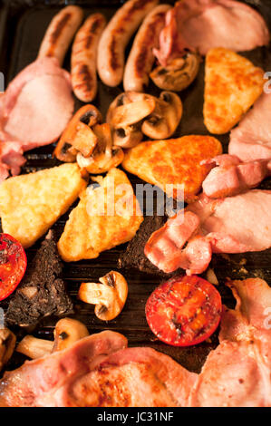 Kochen Frühstück für eine Familie mit einer Nahaufnahme Draufsicht von Speck, Hash Browns, Würstchen, Tomaten und Pilze, die auf einer heißen Bratpfanne brutzeln Stockfoto