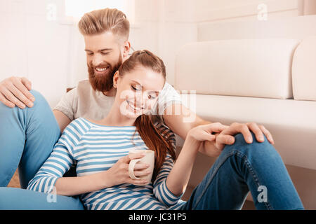 Glückliches junges Paar sitzen zusammen auf Boden und Tee trinken Stockfoto