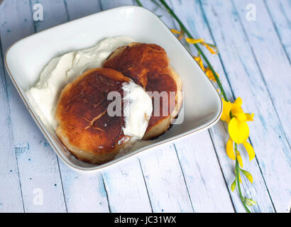 Krapfen mit Käse in einer quadratischen Platte. Gebratene Pfannkuchen auf einem blauen Hintergrund aus Holz Stockfoto