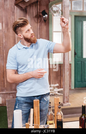 Gutaussehender bärtiger junger Mann mit leeren Glas stehend am Tisch im freien Stockfoto