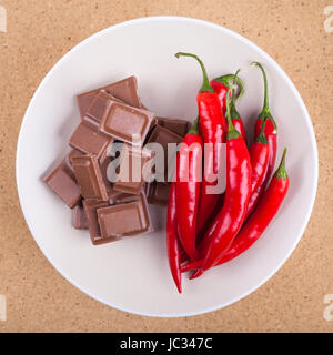 Frische rote scharfe Chilischoten mit Schokolade auf Platte, über hölzerne Hintergrund. Stockfoto