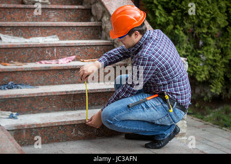 Junge Baumeister Treppe Höhe von Maßband überprüfen Stockfoto