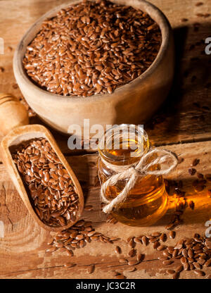 Leinöl, Schüssel und Löffel mit Leinsamen auf hölzernen Hintergrund. Stockfoto