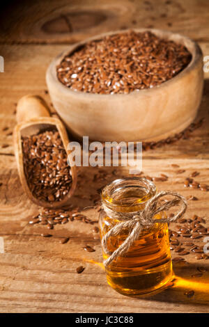 Leinöl, Schüssel und Löffel mit Leinsamen auf hölzernen Hintergrund. Stockfoto