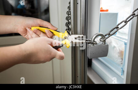 Konzeptionelle Foto von Frau versucht, die Kette am Kühlschrank mit einer Zange zu schneiden Stockfoto