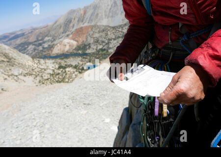 Eine Nahaufnahme von einer Frauenhand, wie sie eine Wegbeschreibung vor führt einen Stellplatz auf einer langen alpinen Kletterroute auf Mt. Goode, High Sierra California liest. Stockfoto